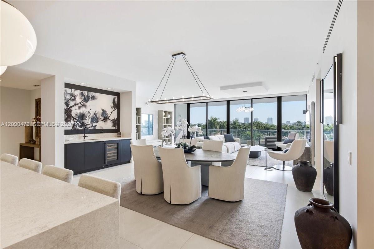 Open-plan dining and living area with cream chairs, a built-in bar, and floor-to-ceiling balcony windows.