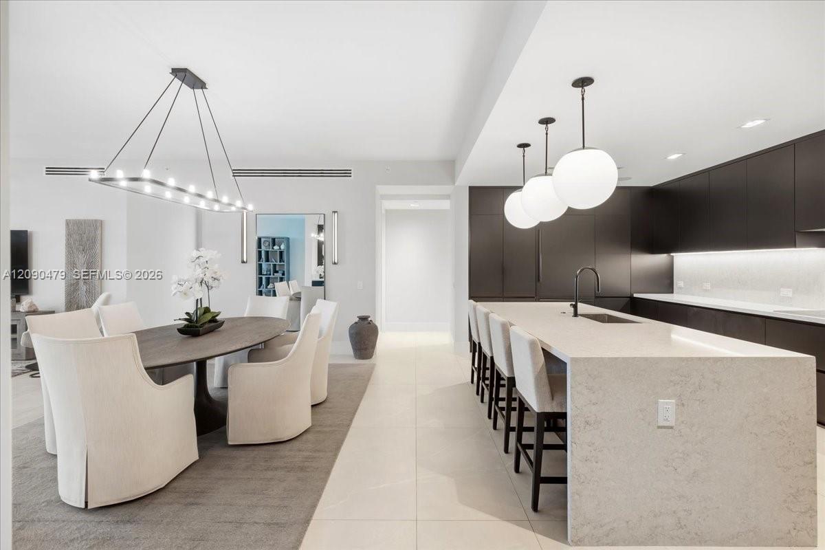 Open-plan kitchen and dining area with a long stone island and dark cabinetry.