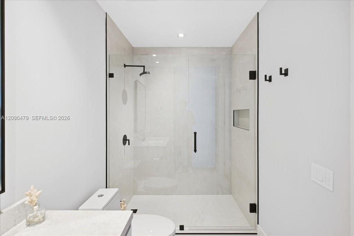 Modern bathroom with a glass walk-in shower, matte black fixtures, and marble vanity counter.