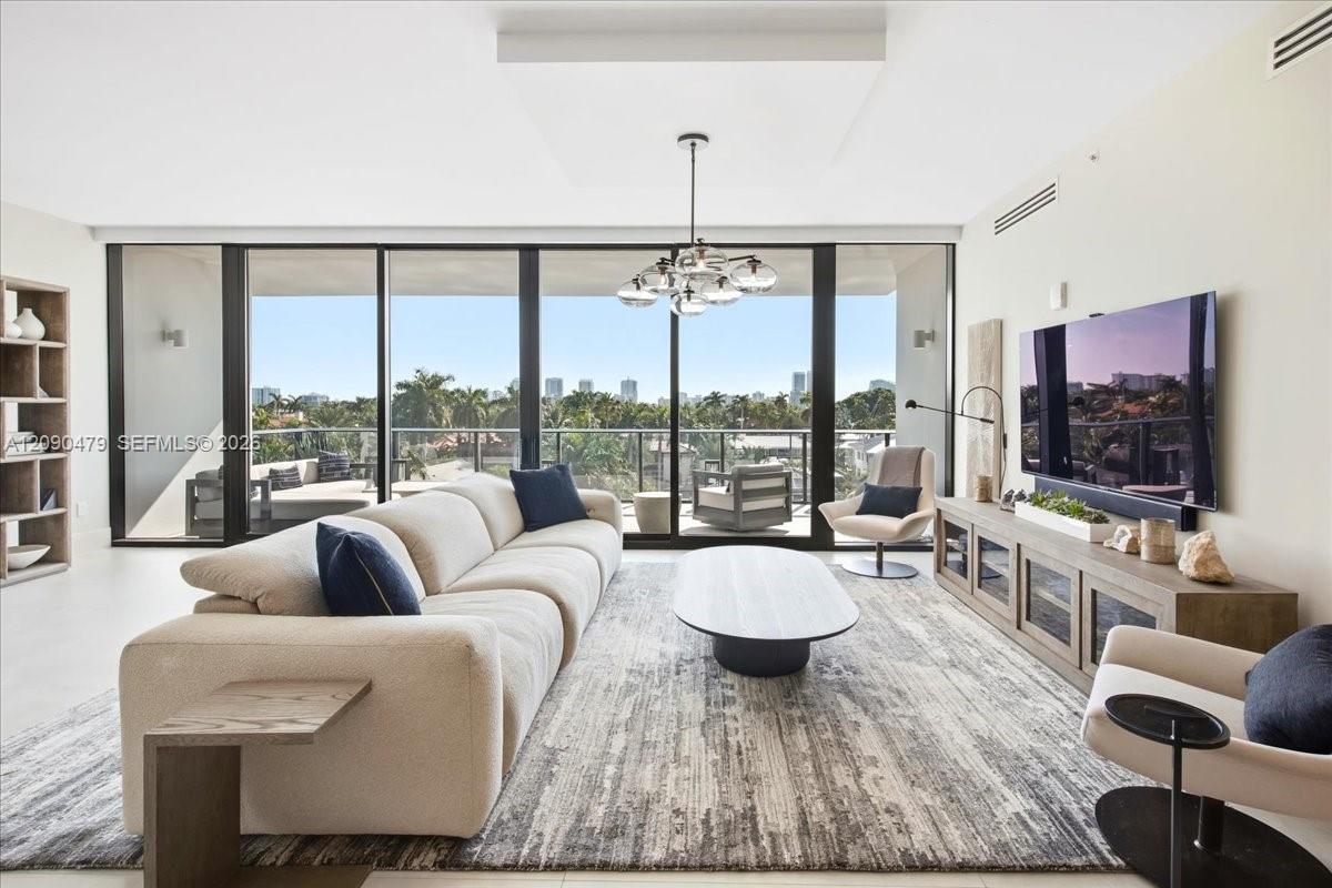 Living room with a curved cream sectional, floor-to-ceiling glass doors, and a balcony overlooking palm trees.