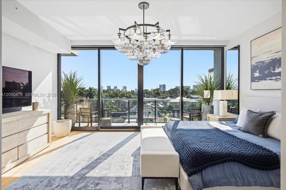 Bright bedroom with a blue knit bedcover and floor-to-ceiling balcony doors overlooking palm trees and the skyline.