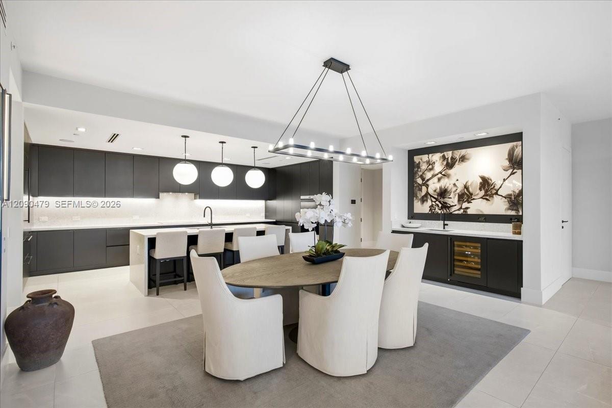 Open-plan kitchen and dining area with dark cabinetry, white island, and round table beneath a modern pendant light.