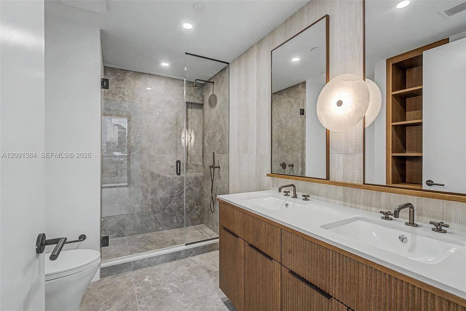 Modern bathroom with a double-sink wood vanity and glass-enclosed gray tile shower.
