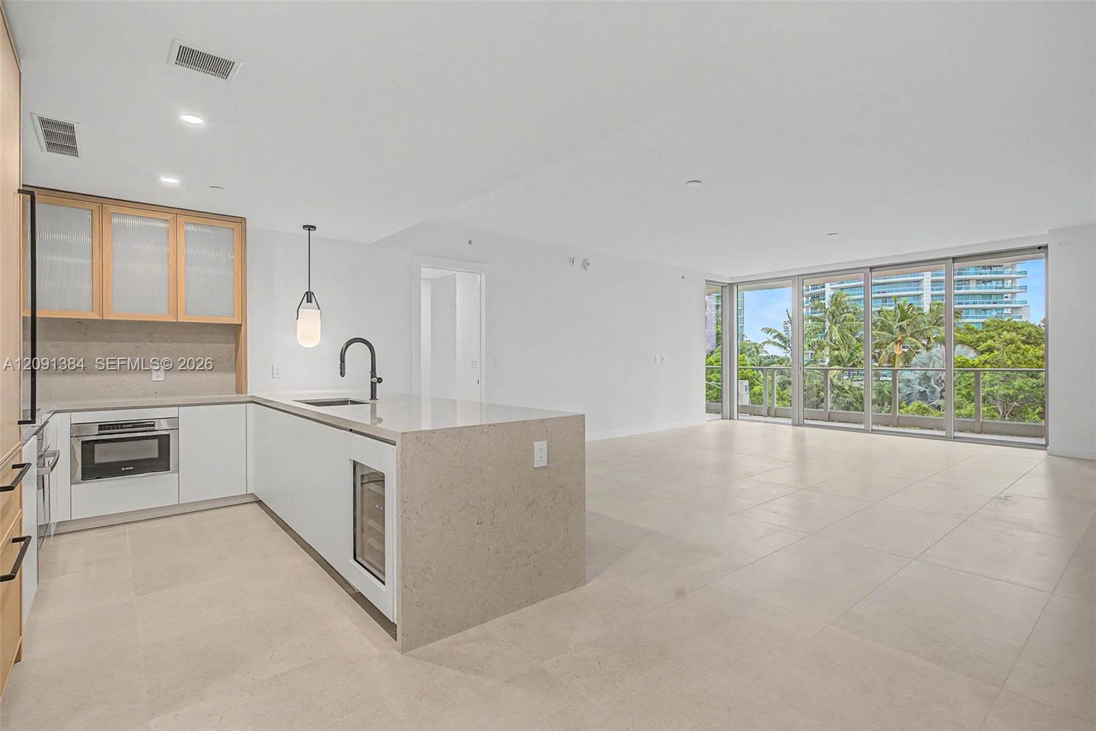 Open-plan condo kitchen and living area with a stone island and balcony windows overlooking palms.