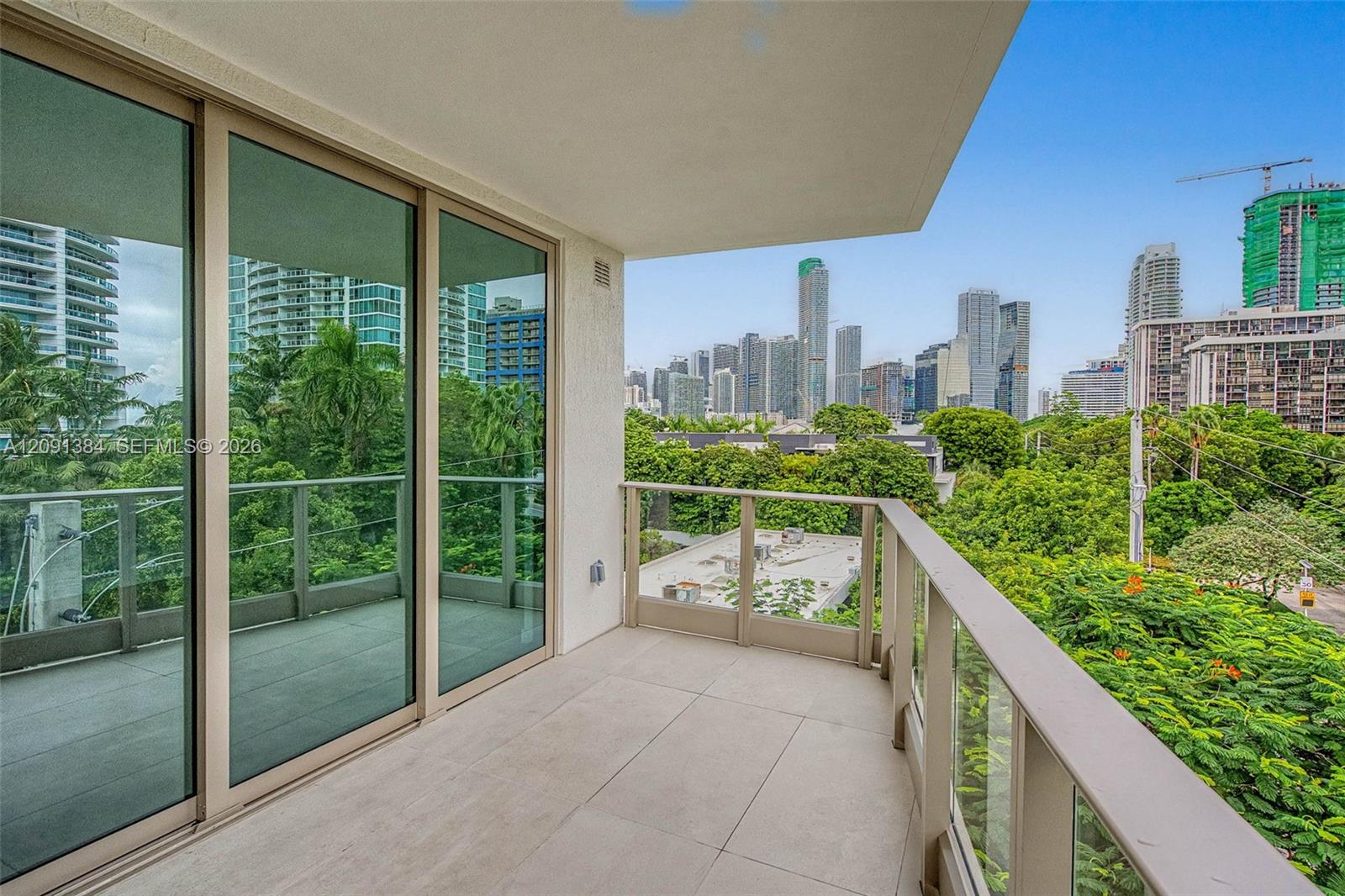 Apartment balcony overlooking green treetops and a city skyline.