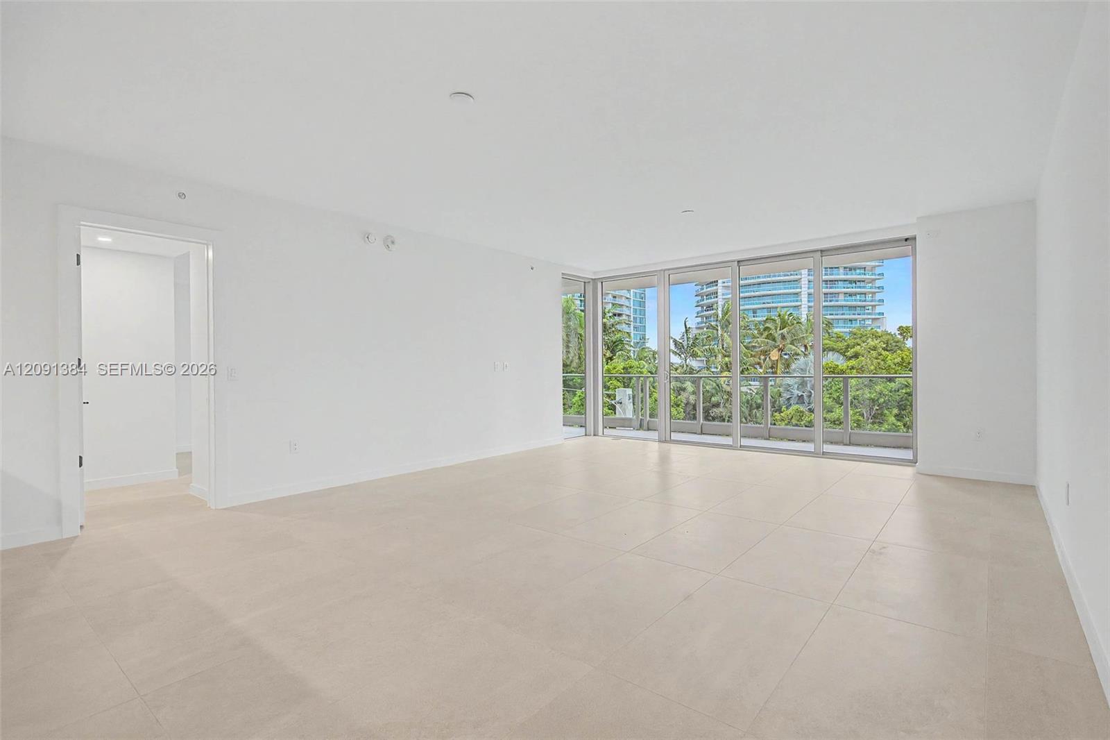 Vacant living room with sliding glass doors opening onto a greenery-lined balcony.