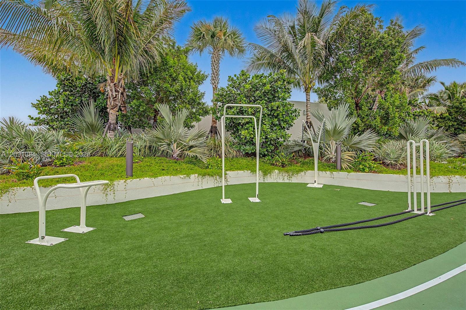 Outdoor fitness area with exercise equipment on turf, surrounded by palms and tropical landscaping.