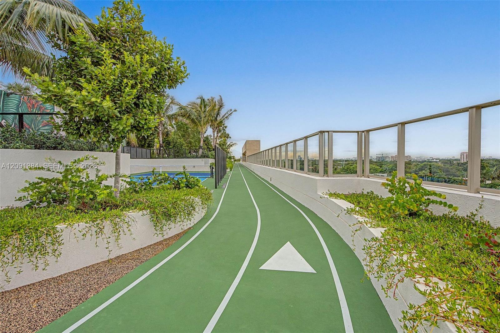Rooftop running track beside landscaped planters, with a pool and city views.