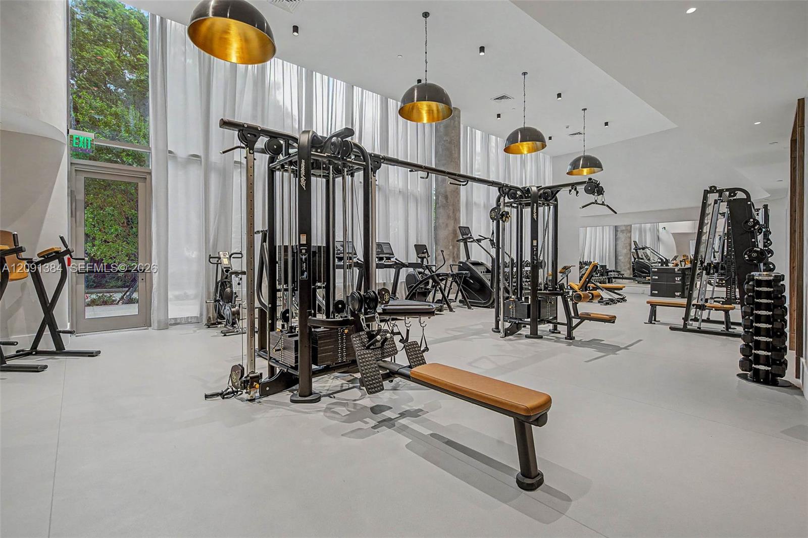 Fitness center with weight machines, dumbbells, and cardio equipment beneath gold pendant lights.