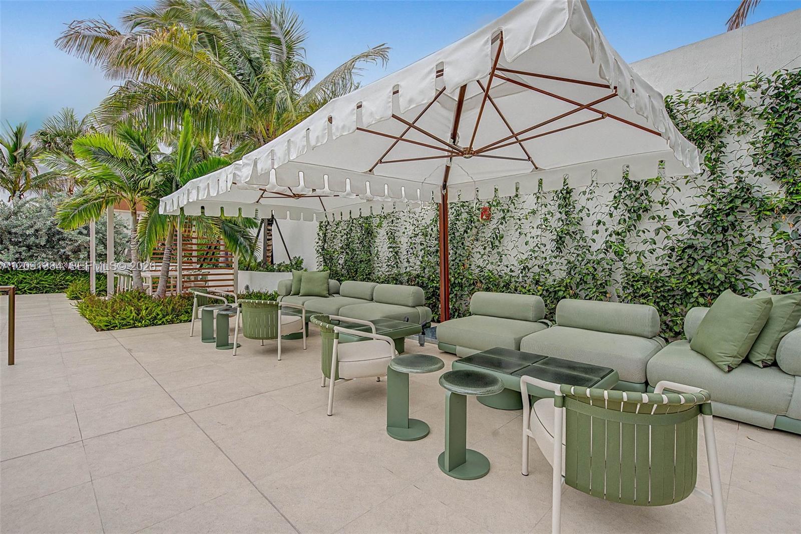 Outdoor patio lounge with pale green seating, white umbrellas, and tropical palms.