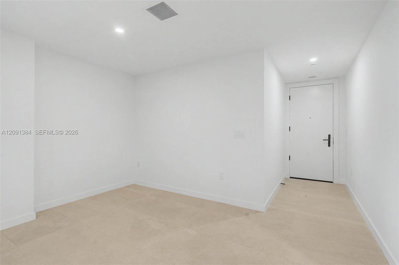 Vacant apartment entry room with pale tile flooring and a white front door.