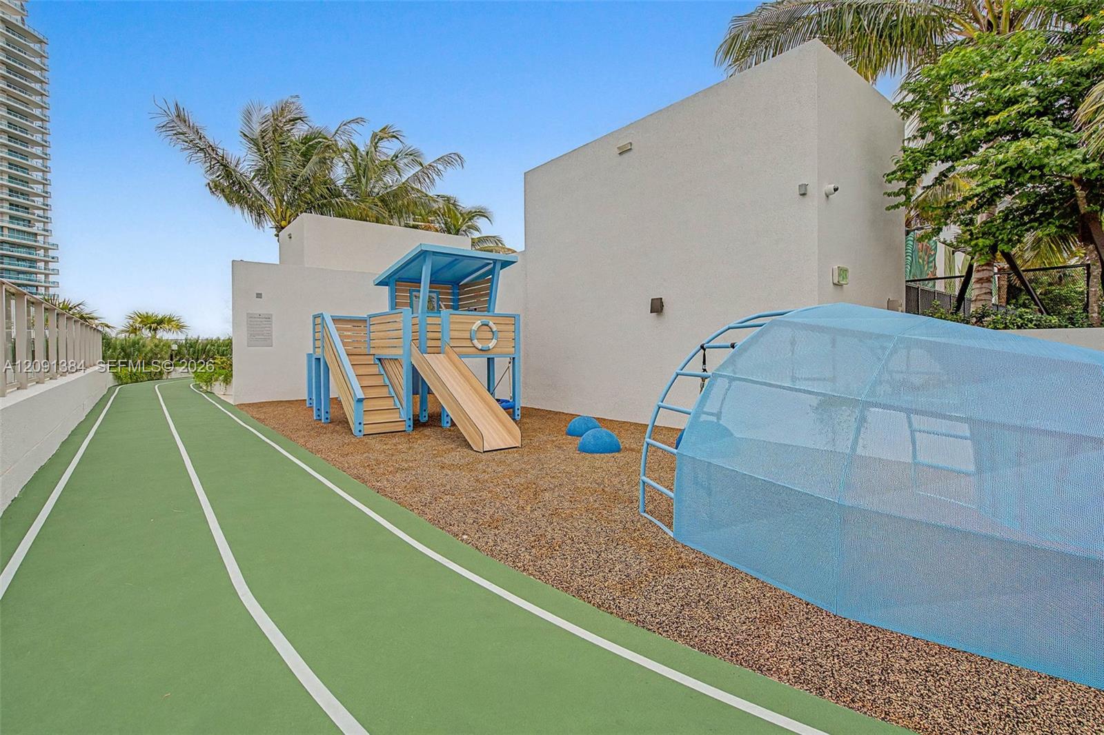 Condominium playground and running track with a wooden slide and blue netted play structure.