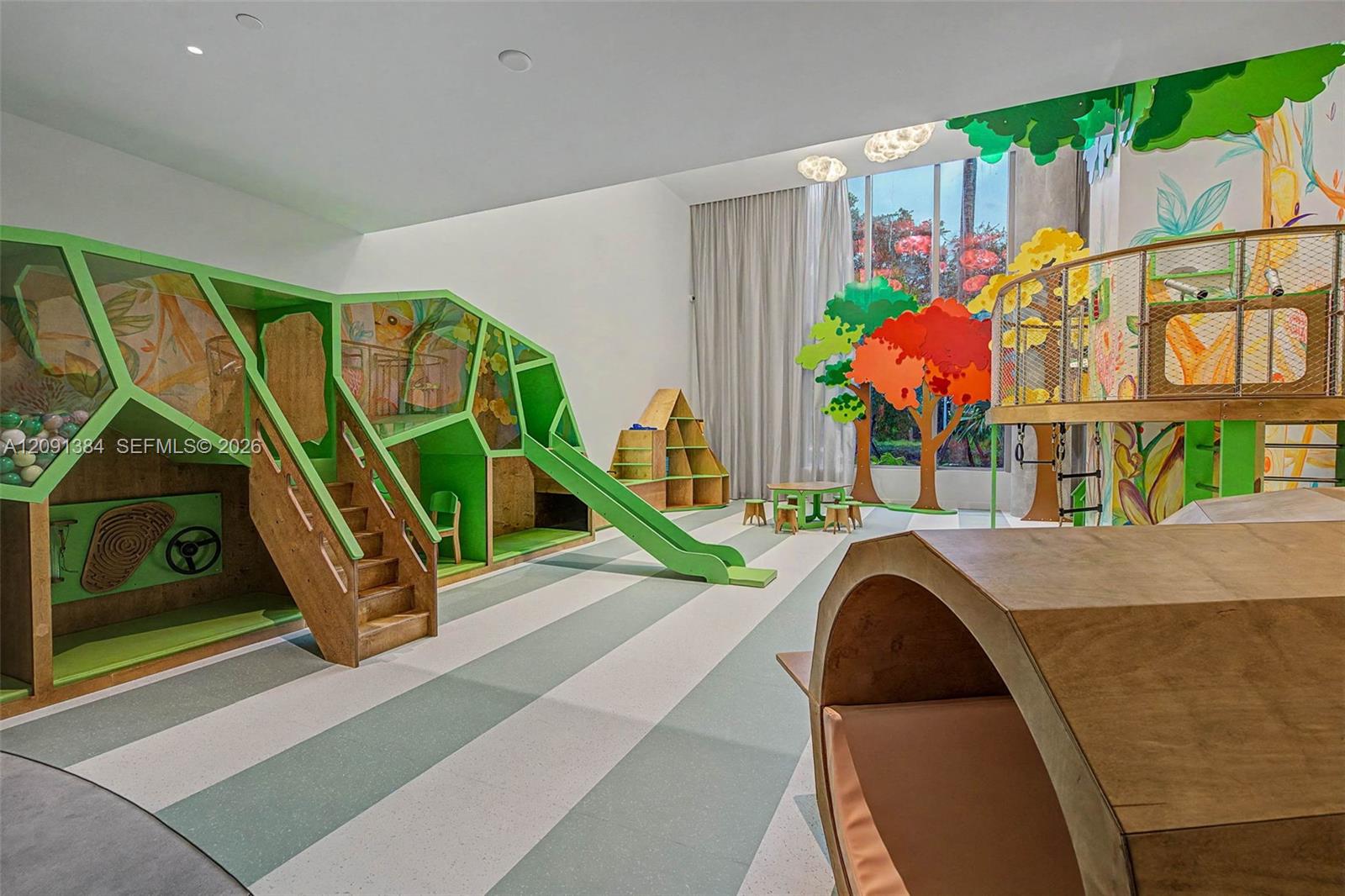 Children’s playroom with a wooden climbing structure, green slide, and colorful tree murals.