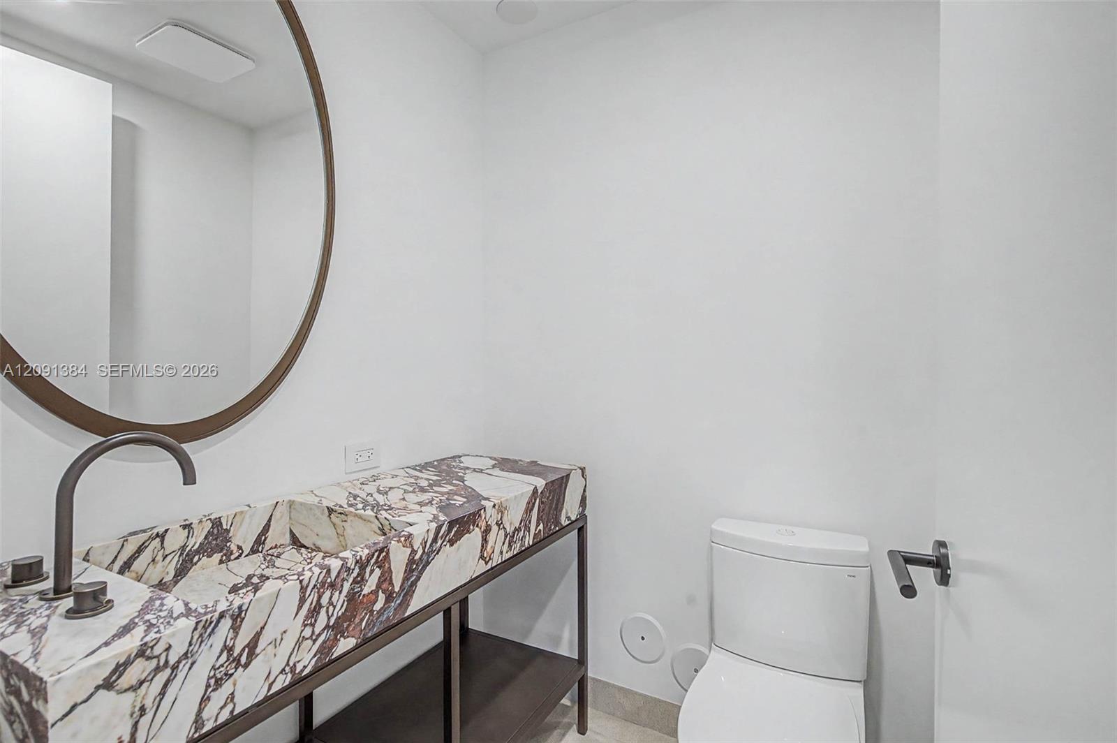 Modern bathroom with a veined marble vanity, round mirror, and white toilet.