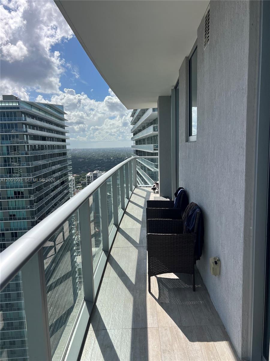 High-rise balcony with wicker chairs, glass railings, and a wide city view.