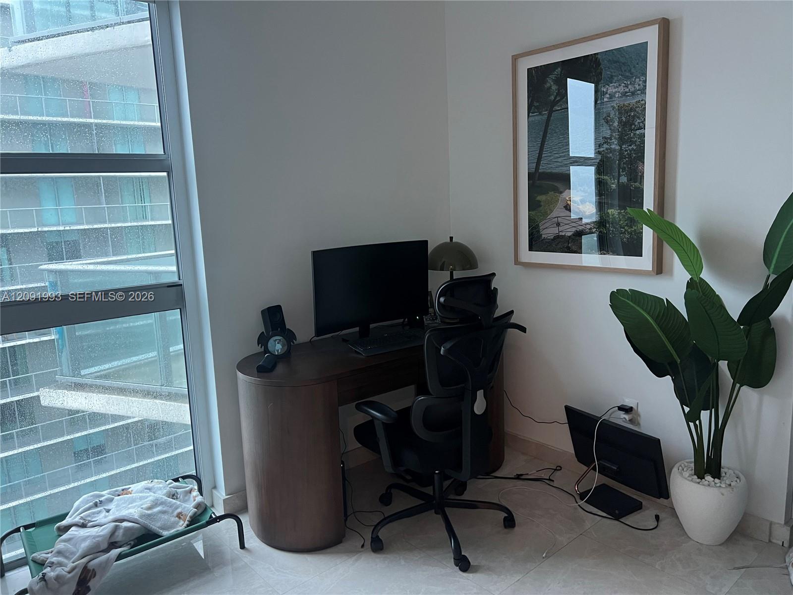Home office nook with a curved desk, ergonomic chair, and large potted plant beside a window.