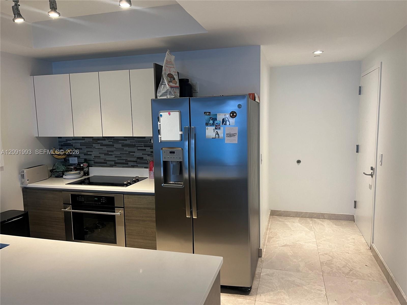 Modern condo kitchen with stainless steel appliances, gray tile backsplash, and a large white island.