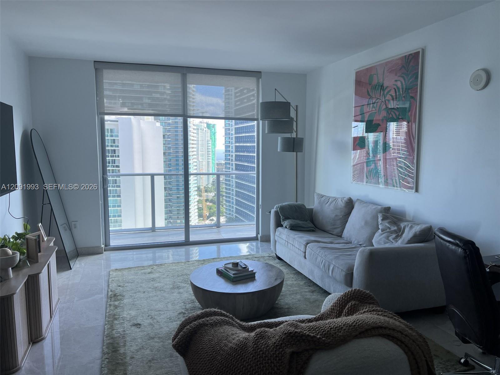 Living room with gray sectional, round coffee table, and sliding glass doors overlooking downtown buildings.