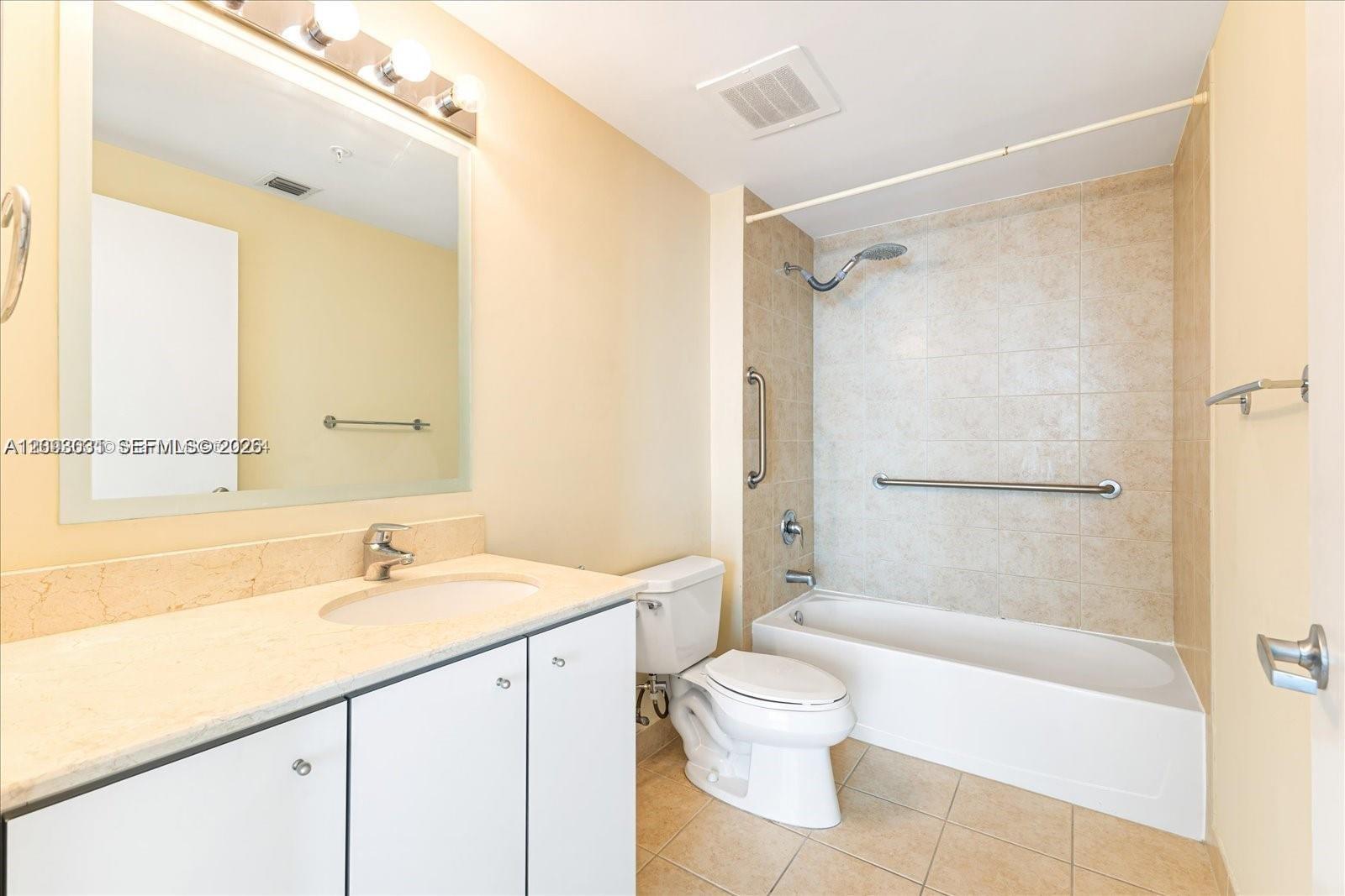 Bathroom with a long white vanity and tiled bathtub with grab bars.