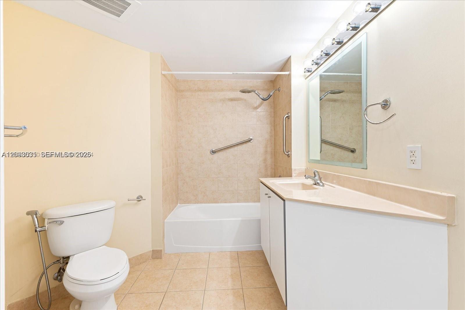 Bathroom with a tiled tub and shower, grab bars, toilet, and long vanity.