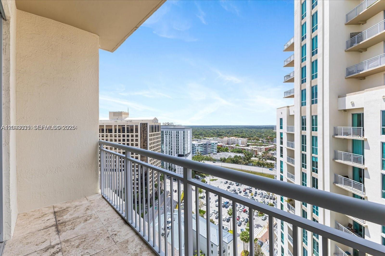 High-rise balcony overlooking nearby buildings and a green urban horizon.