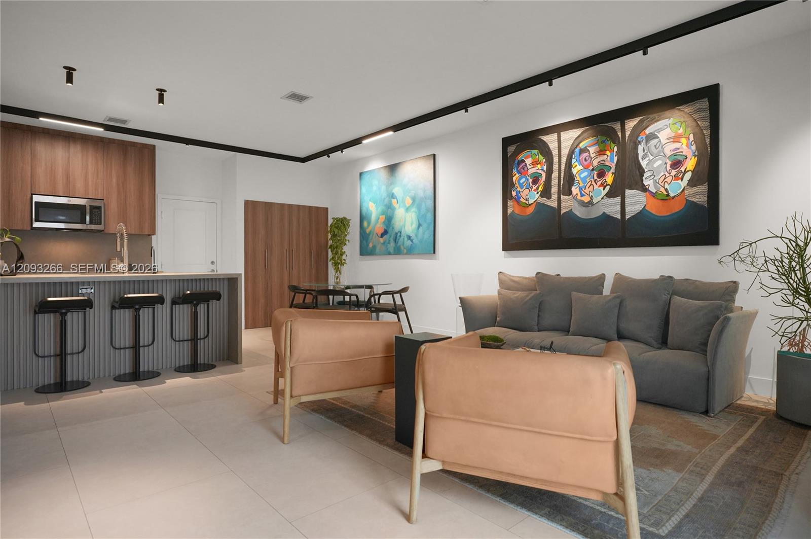 Open-plan living room with a gray sectional, peach chairs, and kitchen with wood cabinetry.