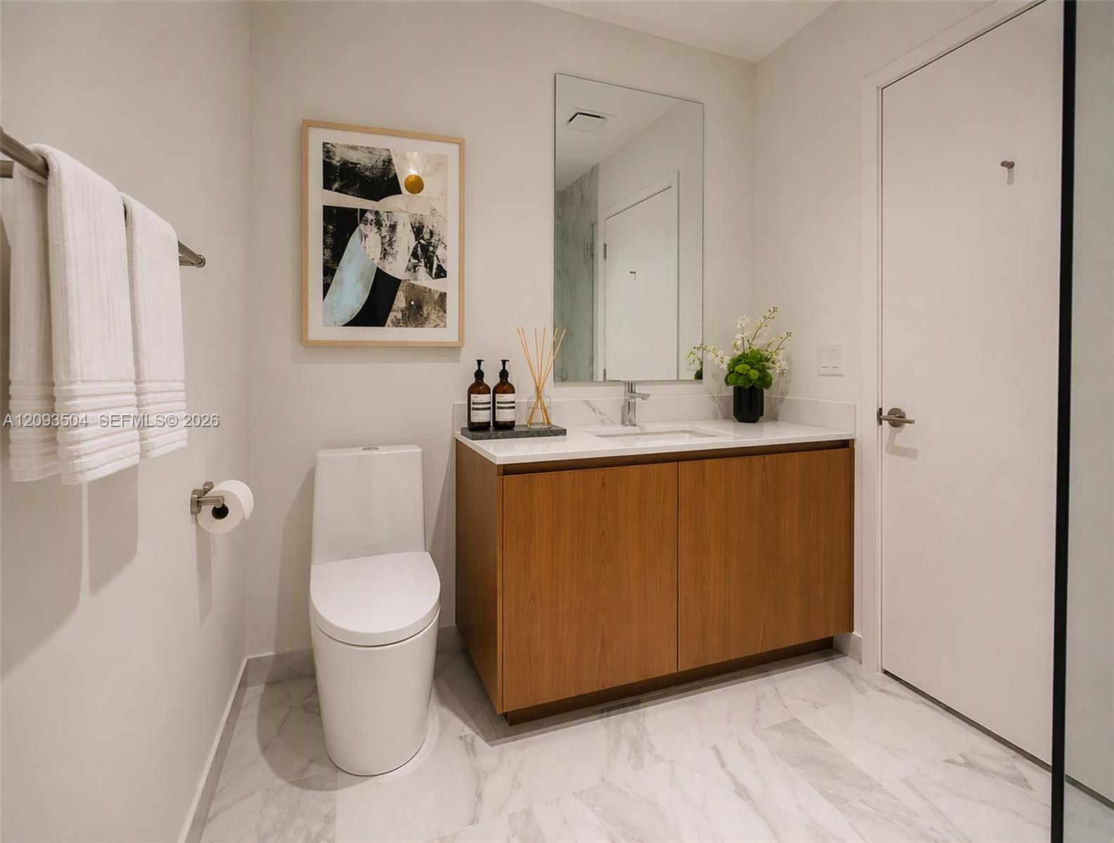 Modern bathroom with a wood vanity, marble counter and floor, large mirror, and white toilet.