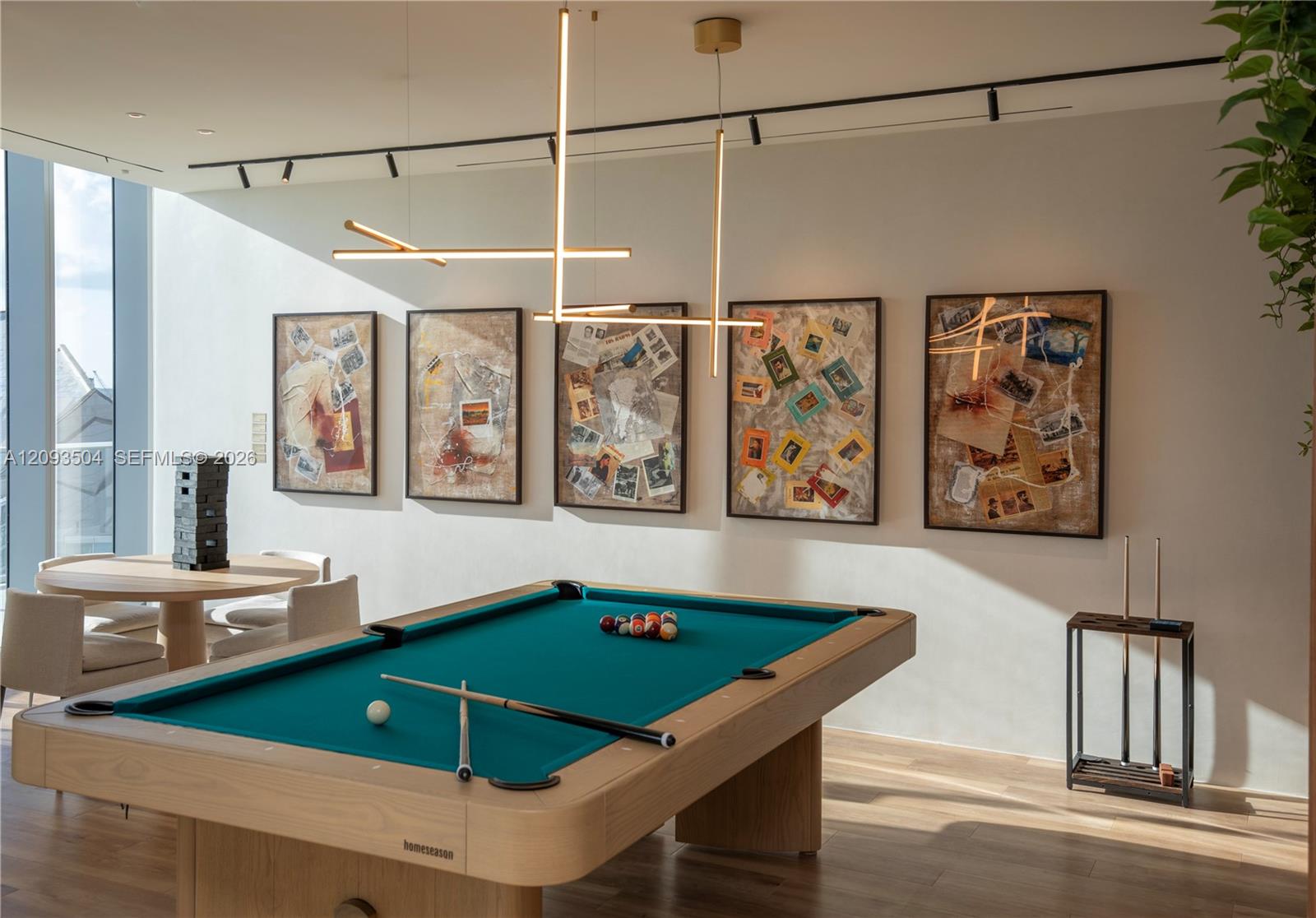 Furnished recreation room with a teal pool table, framed artwork, and a dining nook by tall windows.