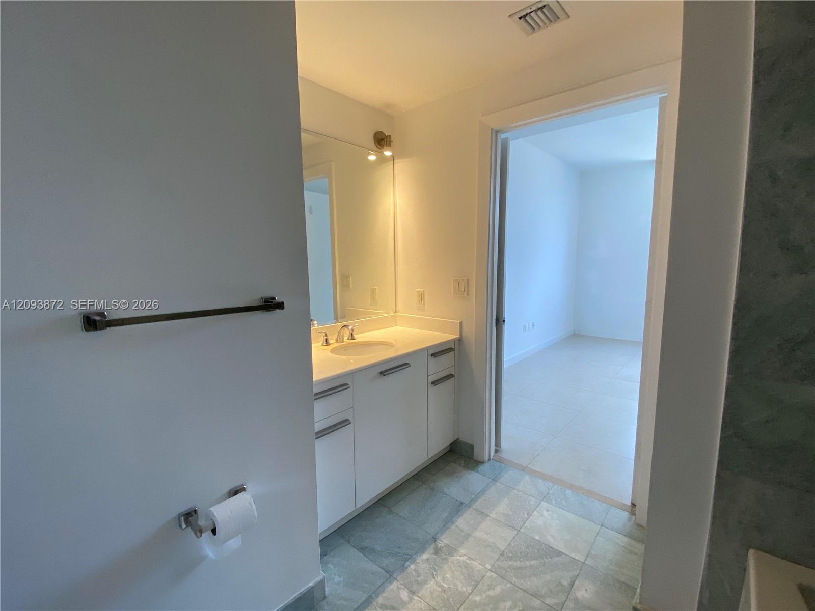 Bathroom vanity and mirror beside an open doorway to an empty room.