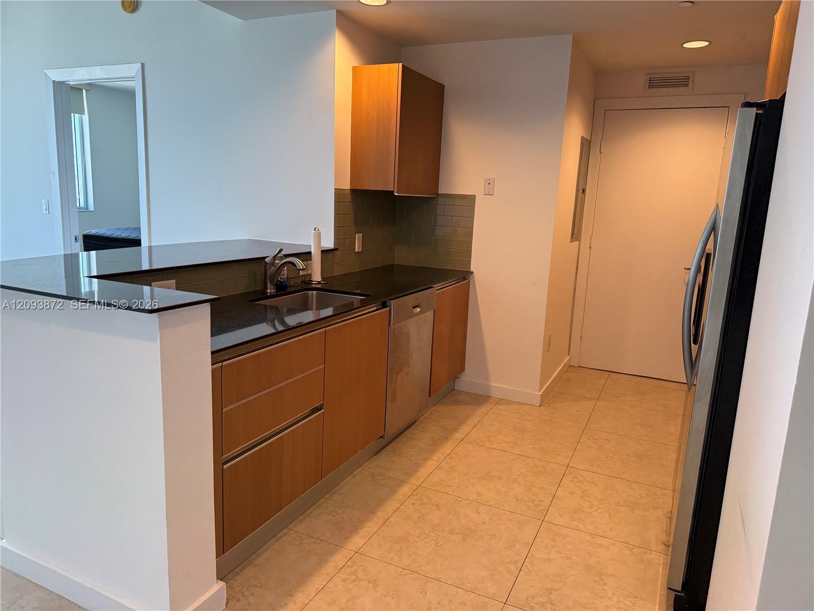 Condo kitchen with dark countertops, wood cabinets, green tile backsplash, and stainless-steel appliances.