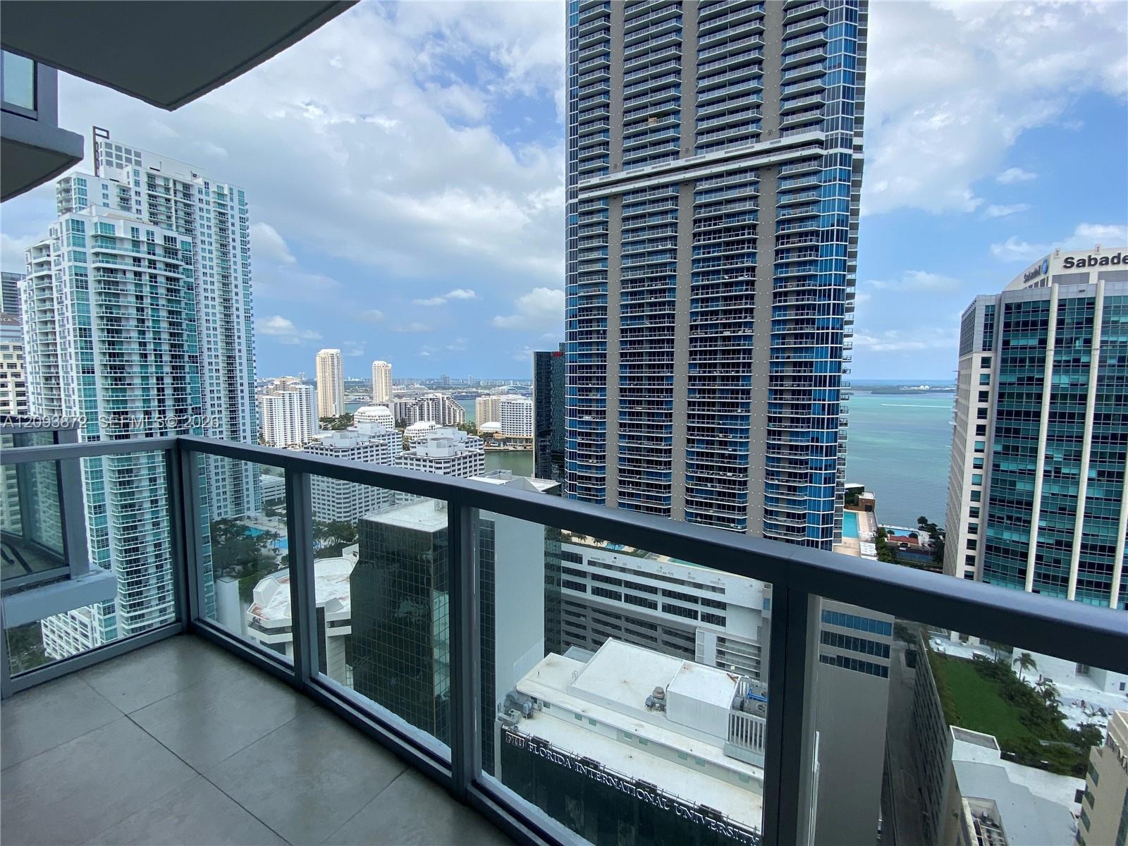 High-rise balcony overlooking Miami towers and water, with Florida International University signage visible below.