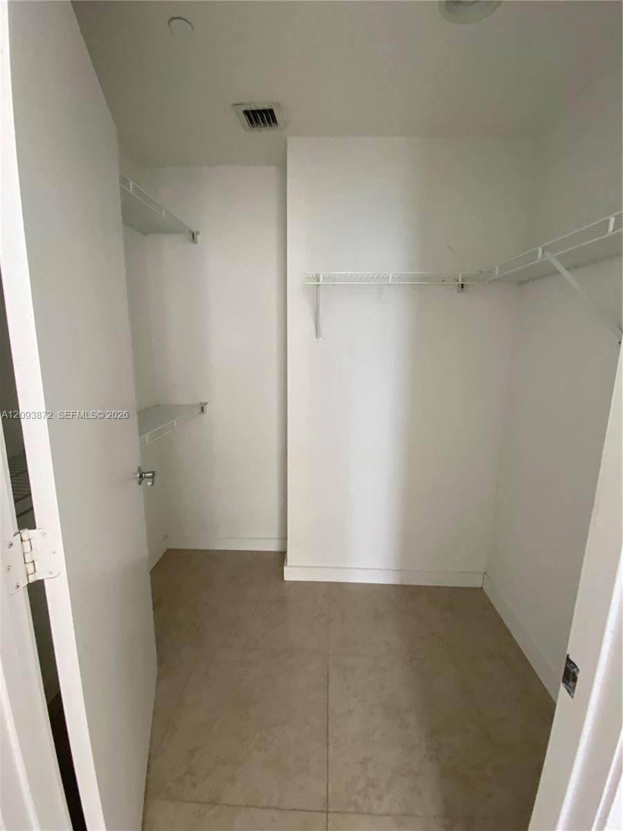 Empty walk-in closet with white wire shelving and beige tile floor.