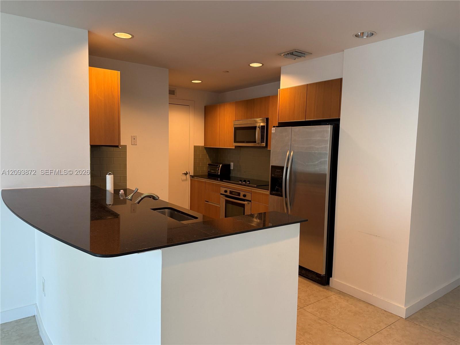 Vacant condo kitchen with wood cabinets, dark stone counters, and stainless steel appliances.