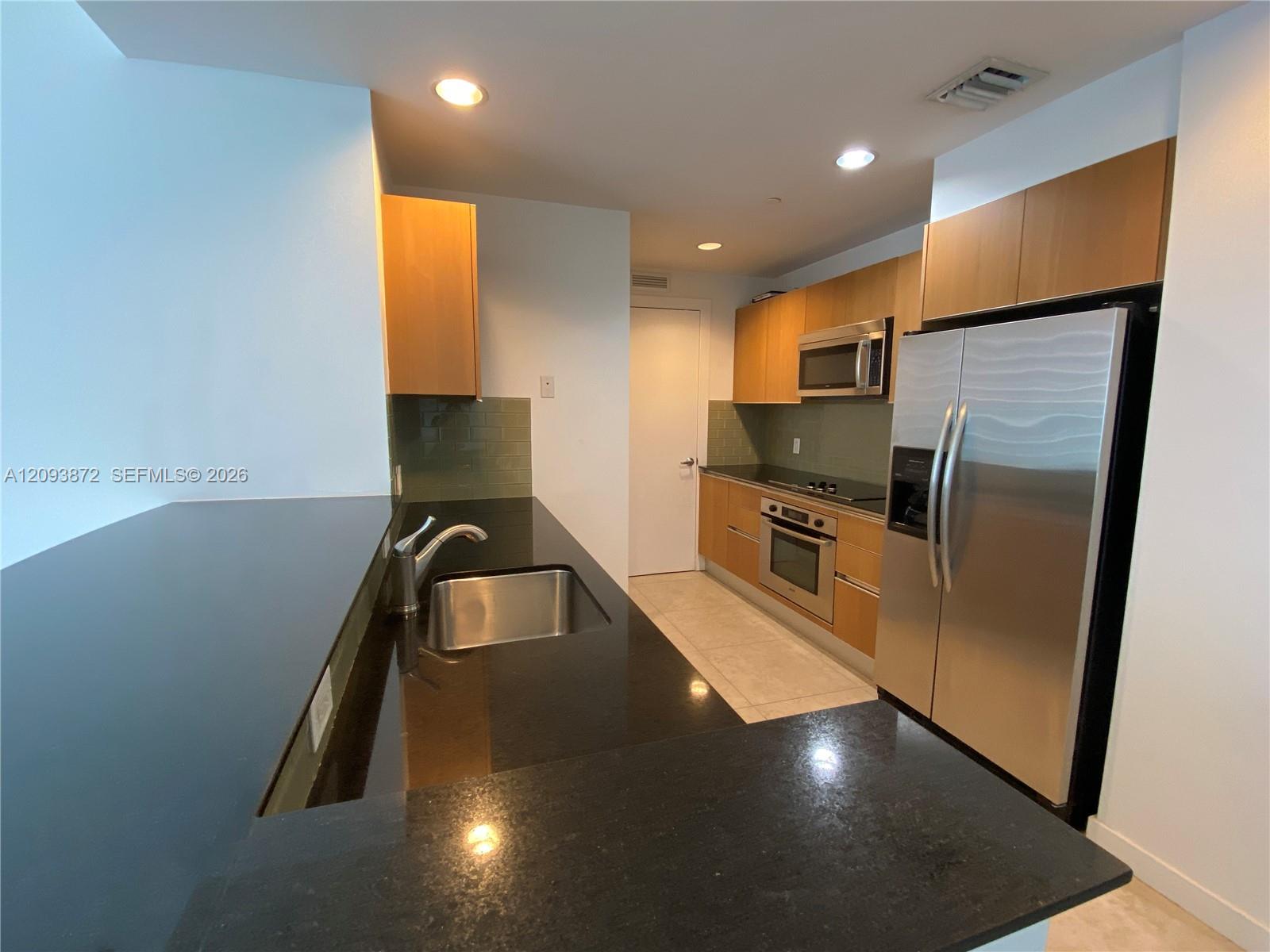Apartment kitchen with dark granite counters, light wood cabinets, and stainless steel appliances.