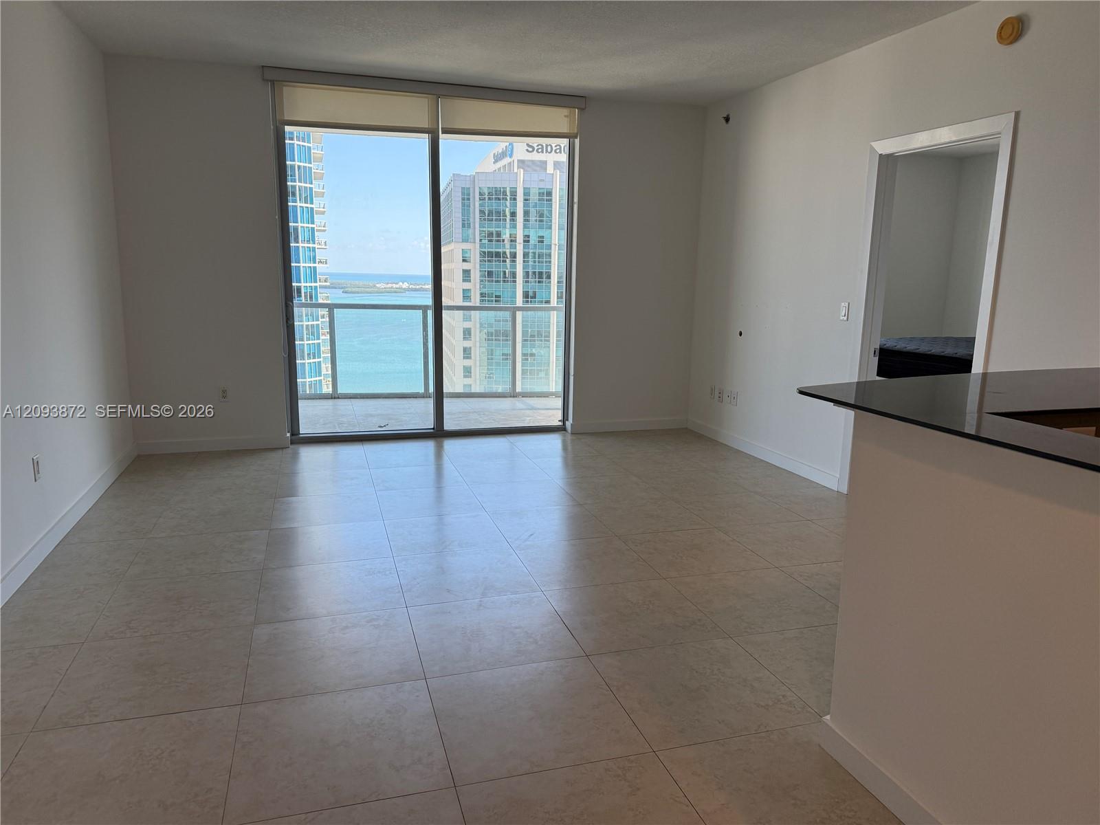 Vacant condo living area with tiled floors, balcony doors, and water views between high-rise buildings.