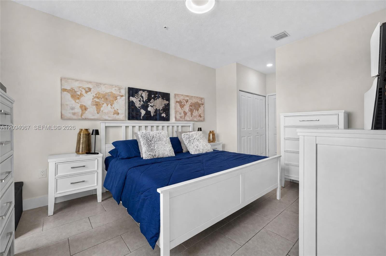 Bedroom with a white bed, vivid blue bedding, gray tile floor, and world map artwork.