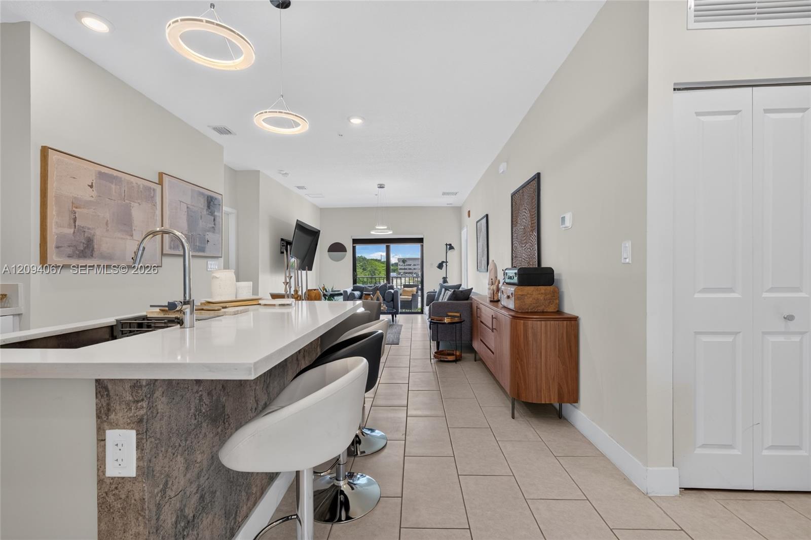 Open-plan kitchen with a long white island and bar stools leading to a living area with glass doors.