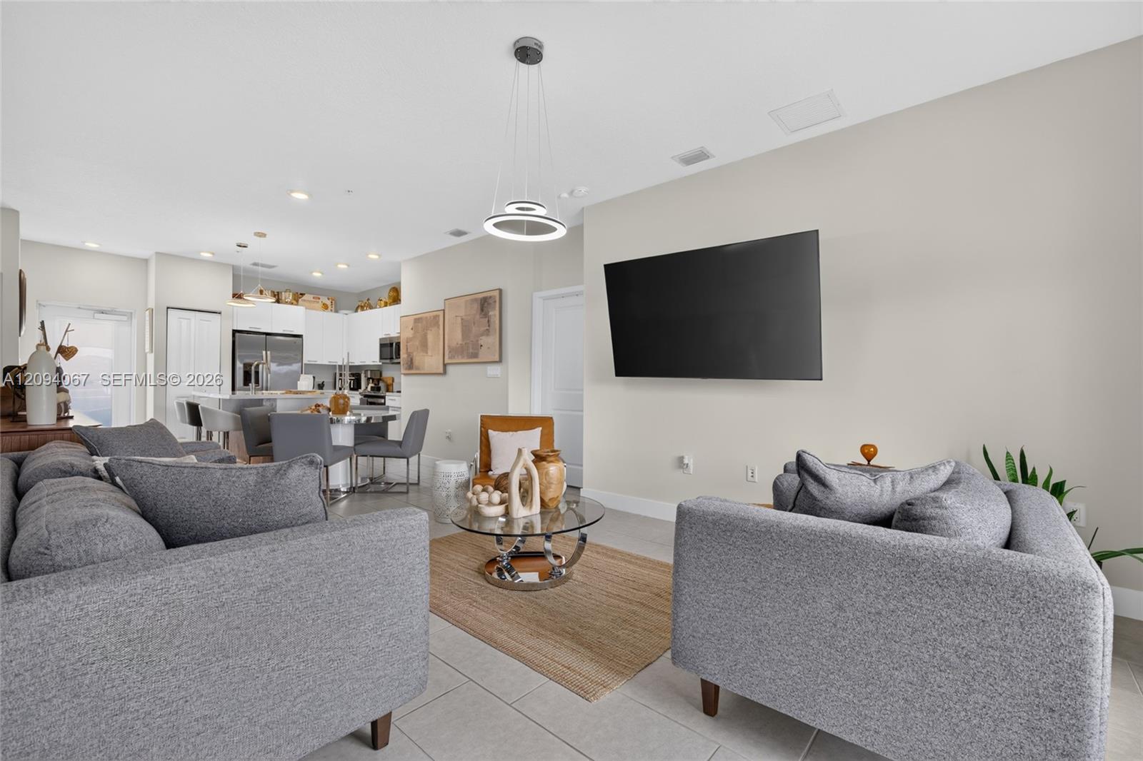 Furnished living room with gray sofas, glass coffee table, and an open kitchen.