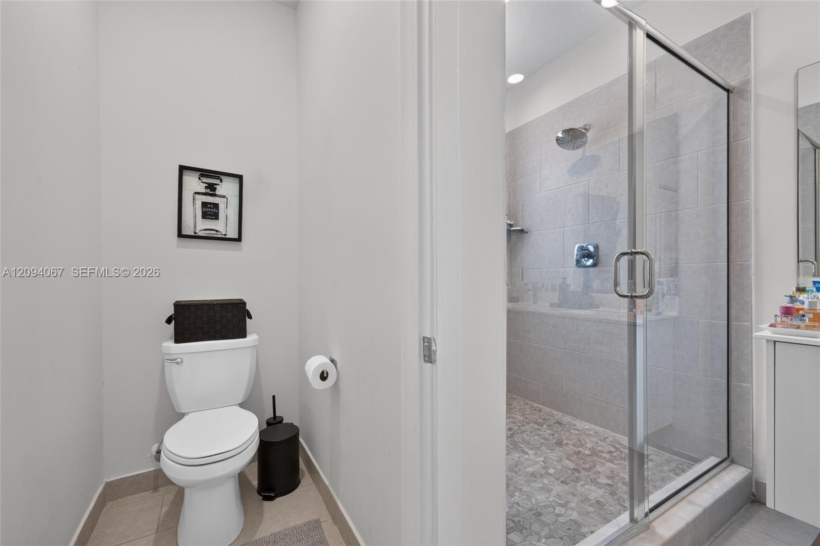 Bathroom with a glass-enclosed gray-tiled shower beside a toilet.