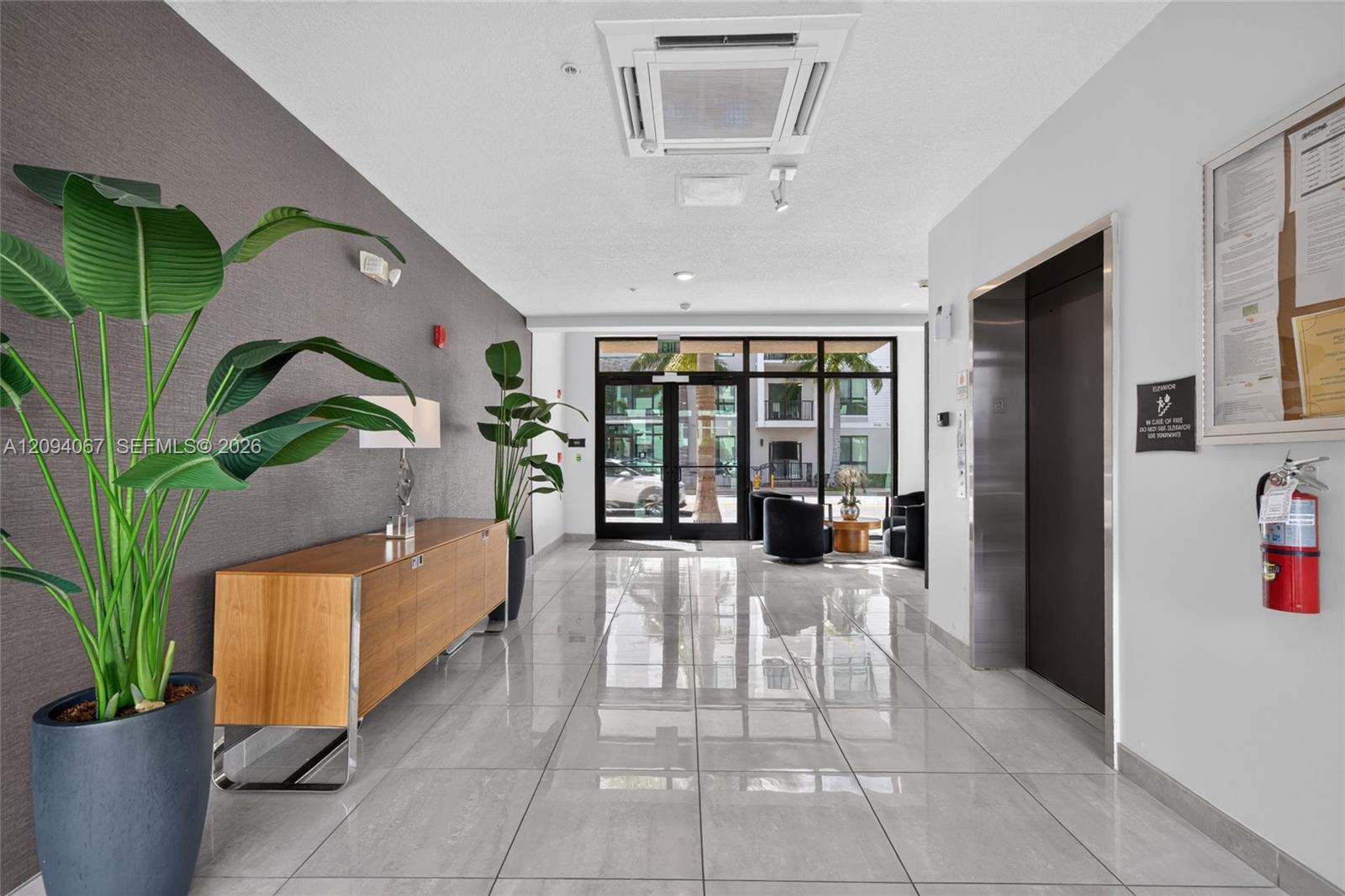 Apartment lobby with glossy tile floors, a wood console, tropical plants, and an elevator.
