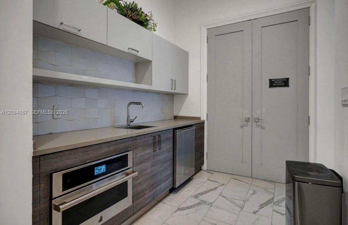 Compact kitchen with a built-in oven, under-counter refrigerator, and mechanical-room doors.