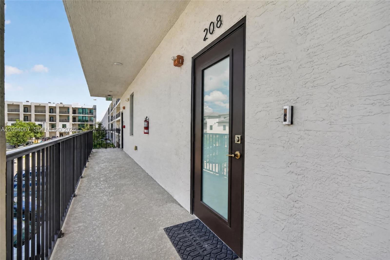 Unit 208 entrance along an elevated corridor with a glass door and black metal railing.
