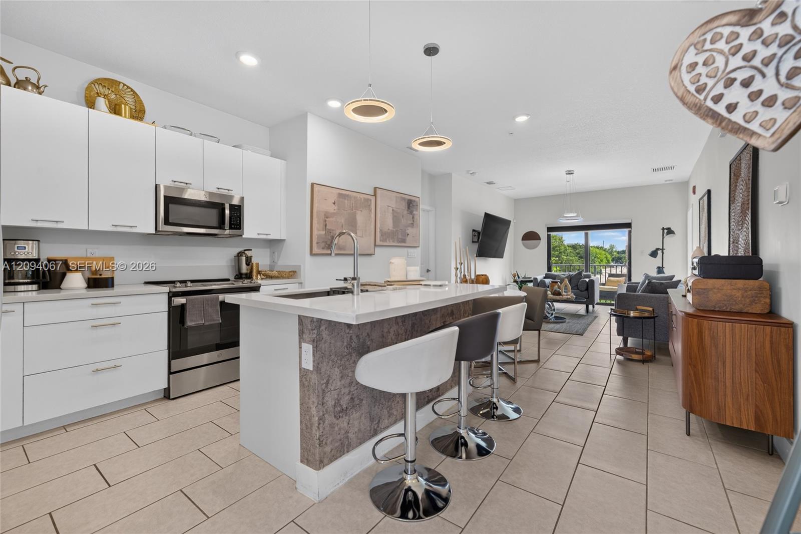 Open-plan kitchen and living area with a large island, bar stools, and balcony views of greenery.