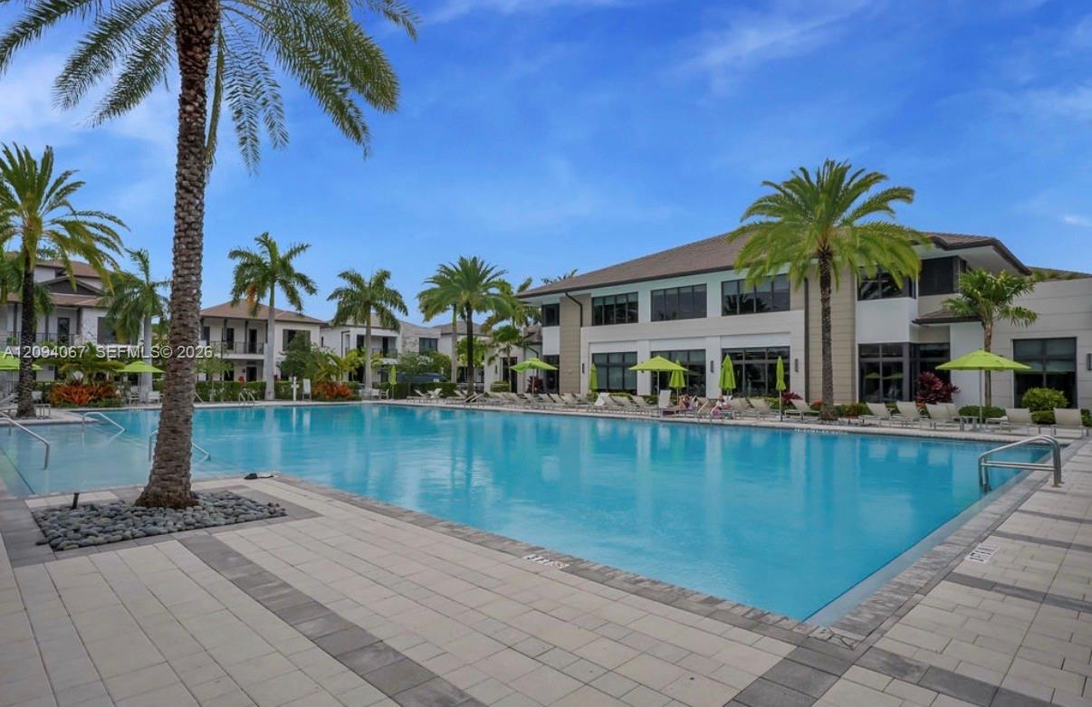 Outdoor pool surrounded by palm trees, lounge chairs, and modern residential buildings.