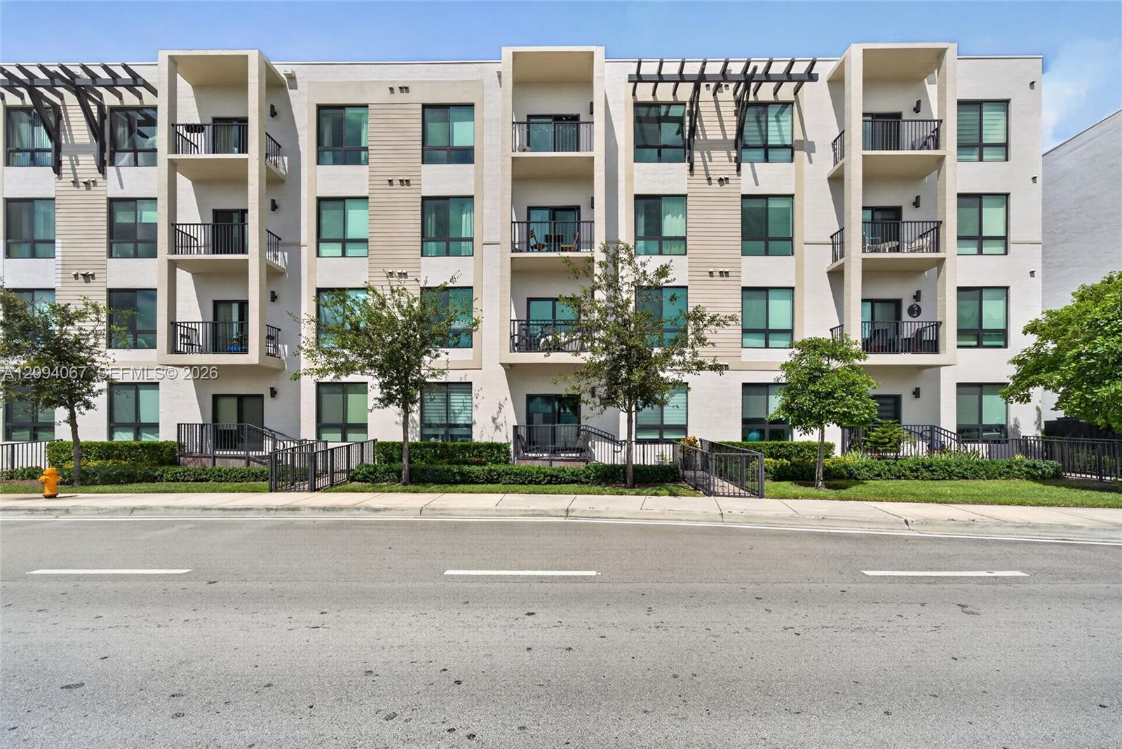 Modern apartment building with projecting balconies and pergola shades, viewed from across the street.