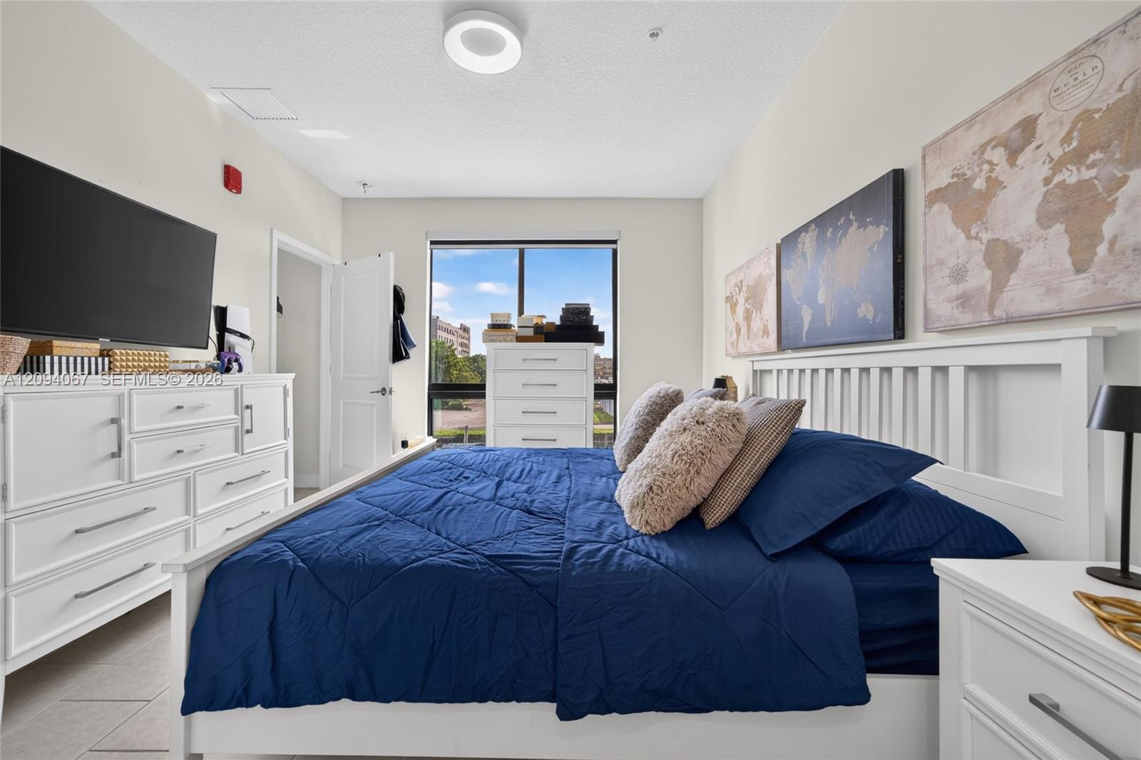 Bedroom with a blue bedspread, white furniture, world map art, and a large window.