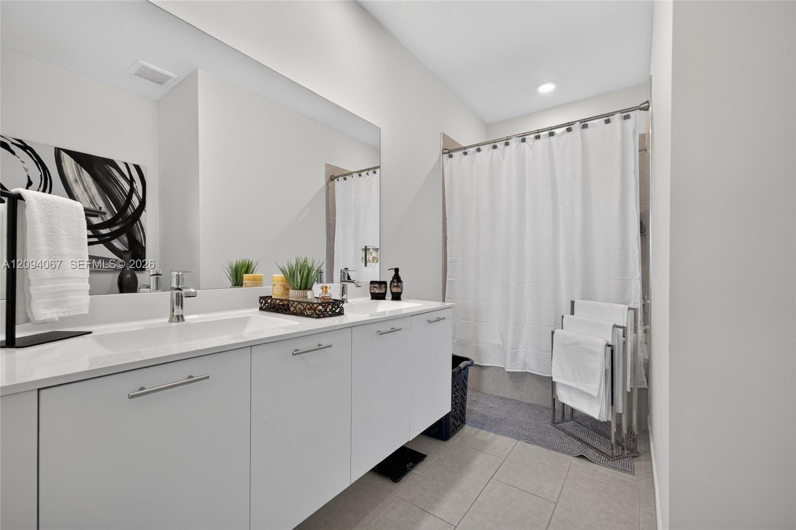 Bathroom with a double-sink vanity, broad mirror, gray tile floor, and white shower curtain.