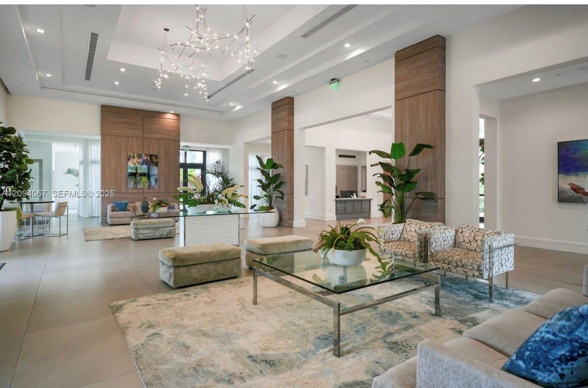 Modern lobby lounge with patterned sofas, wood-paneled columns, indoor plants, and sculptural chandeliers.