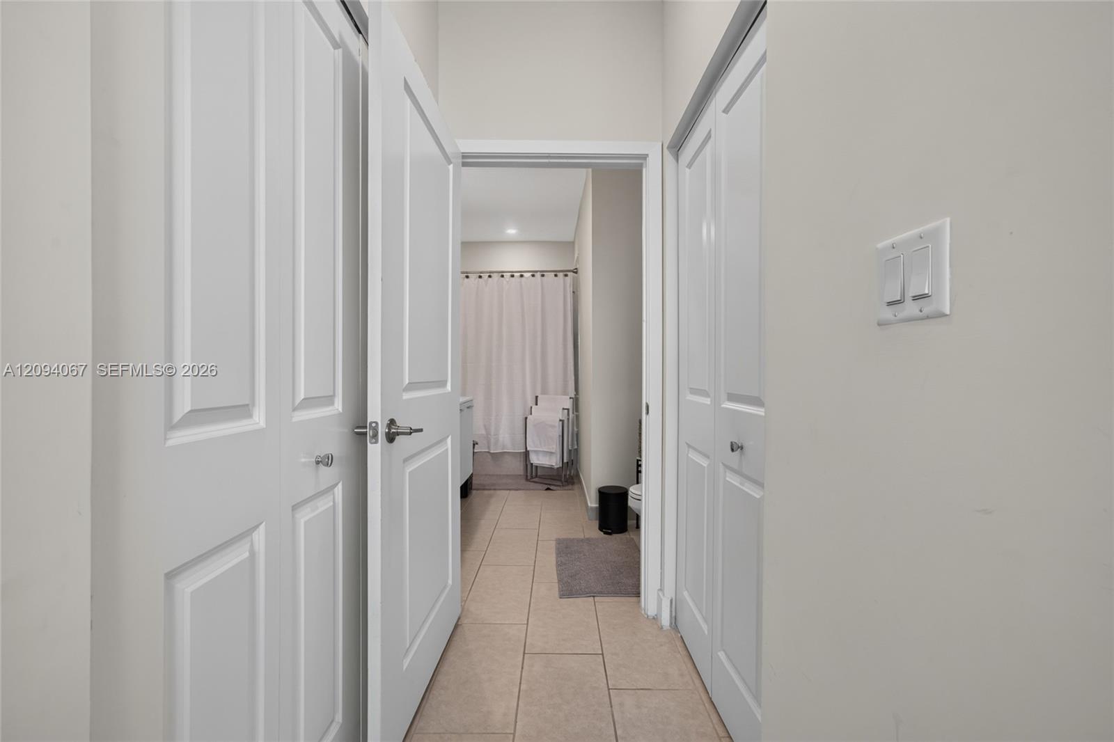 Tiled hallway looking into a bathroom with a shower curtain and folded towels.