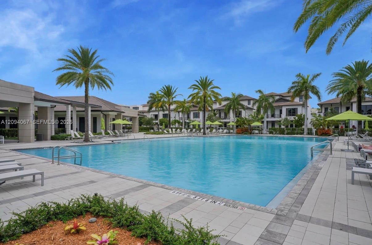 Outdoor swimming pool surrounded by palm trees, lounge chairs, and apartment buildings.